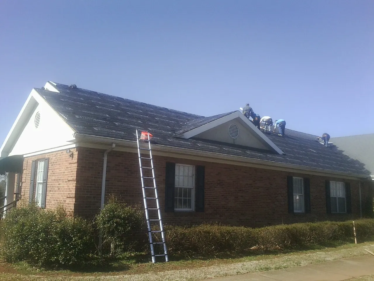 Crew tearing shingles off a brick ranch roof with a ladder set — Emergency Roof Repair work by our crew in New Tazewell