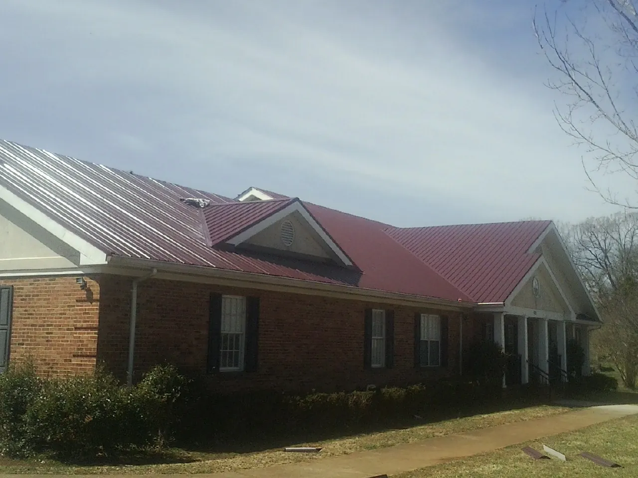 Red metal roof with gabled entries on a long brick building, from a Hail Damage Roof Repair job in New Tazewell