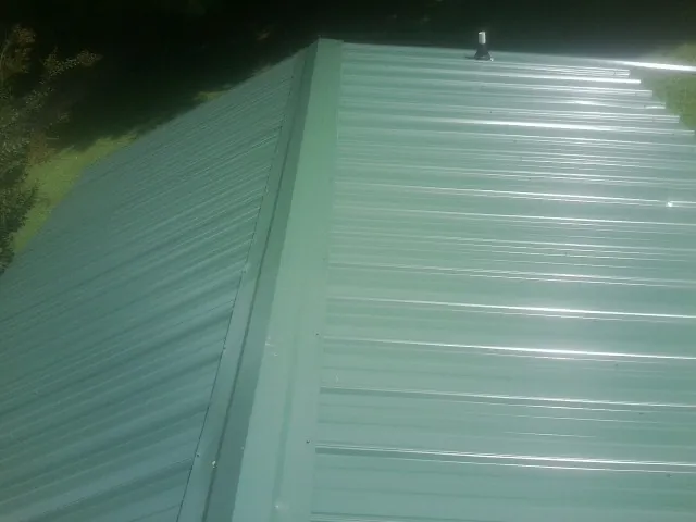 New green metal panels meeting at the ridge of a roof — Flat Roof Repair work by our crew in New Tazewell