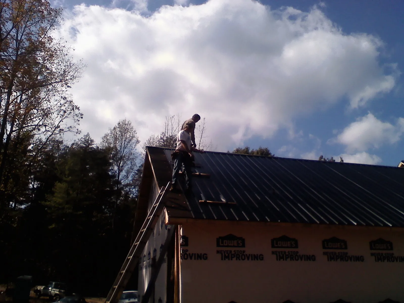 Roofer fastening dark metal panels high against a cloudy sky, from a Roof Inspection job in New Tazewell
