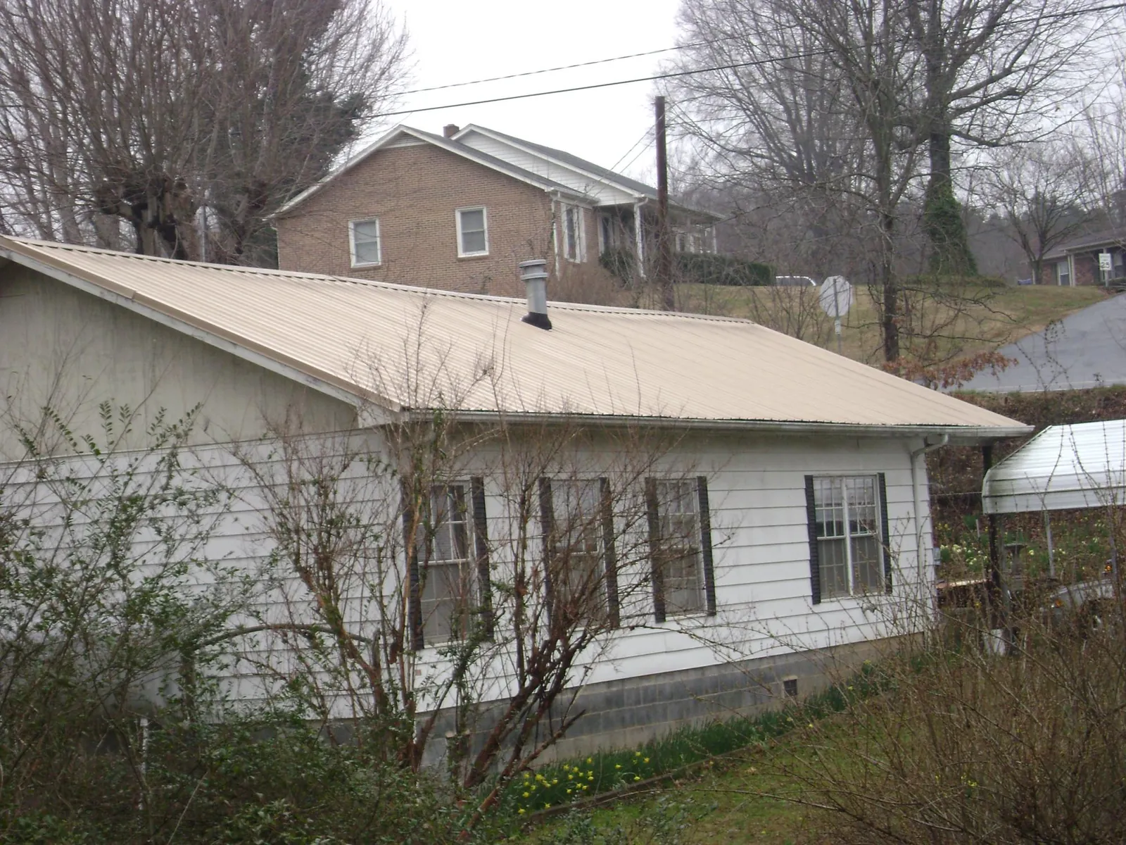 Tan metal roof on a white sided house set into a hillside — Commercial Roofing by Roofing Brothers in New Tazewell
